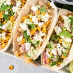 Tacos with chicken, corn, and cheese on a white plate.
