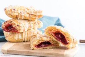 Cherry turnover cut in half on a wooden cutting board with 3 turnovers stacked beside it.