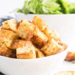 Croutons in a white bowl with salad in the background