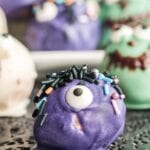 Peanut butter ball coated in purple chocolate with candy eye and sprinkles.