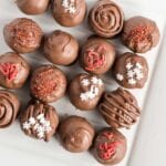Overhead image of various decorated truffles on white platter.
