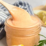 Spicy mayo in a mason jar being scooped with a small wooden spoon.