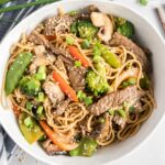 Beef, noodles and vegetables in a white bowl, garnished with sesame seeds.