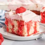 Piece of raspberry cake with pink frosting, white sprinkles and fresh raspberries on top.