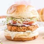 Salmon burger on brioche bun topped with tomato, sprouts and onion.
