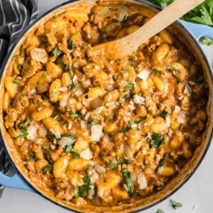 Gnocchi with sausage and red pesto in a blue skillet.