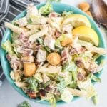 Caesar salad with chicken, bacon and pasta in a blue serving bowl.