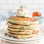 Stack of pancakes topped with whipped cream and rainbow sprinkles.