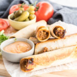 Taquitos on a wooden cutting board with burger sauce in a dipping bowl.