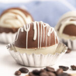 Hot chocolate bomb with white chocolate on bottom and milk chocolate on top drizzled with white chocolate.