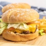 Cheeseburger with lettuce and tomato on a wooden cutting board.