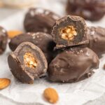 Chocolate covered dates in a stack with one cut in half showing it filled with chopped almonds.