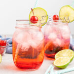 Shirley Temple cocktail in mason jar glasses garnished with lime wedge, a cherry, and paper straw.