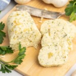 Garlic compound butter on a wooden cutting board cut into slices with a butter knife.