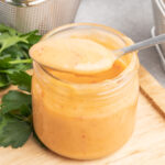 A spoonful of bang bang sauce propped on the rim of a jar of sauce.