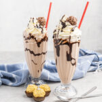 Two Ferrero milkshakes in tall glasses with chocolate sauce, whipped cream and Ferrero Roche ball.
