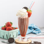 Strawberry milkshake with Oreo cookies, topped with whipped cream a fresh strawberry and an Oreo with two straws.