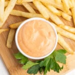 Boom boom sauce in a small white bowl on a wooden board with crispy French fries.