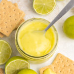 Lime curd in a small mason jar with sliced limes and graham crackers on the table.