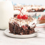 Slice of Chocolate cake topped with cherry pie filling, cool whip and chocolate sprinkles.