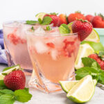 Two drinks with strawberries, lime and club soda in short glasses with ice.