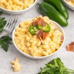 A small bowl of Mac and cheese topped with jalapeno slices and crumbled bacon.