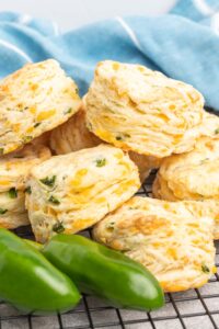 A pile of biscuits on a cooling rack with some jalapeno peppers.