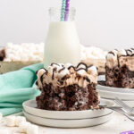 A piece of chocolate cake filled topped with chocolate whipped cream, chocolate sauce and mini marshmallows.