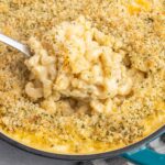 A skillet of Mac and cheese with toasted bread crumbs and a serving spoon removing a scoop.