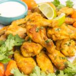 Habanero hot wings on a plate with lime wedges, habanero peppers, and blue cheese dip.