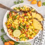 A bowl of pineapple salsa with pineapple wedges, half a lime and whole habaneros on the side.