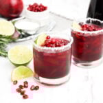 Pomegranate margarita in a short glass garnished with pomegranate seeds, lime wedge and a salted rim.