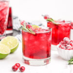 Two cranberry margaritas in cocktail glasses garnished with rosemary sprigs and sugared cranberries.