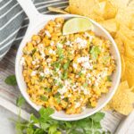 A bowl of corn dip with feta cheese and cilantro surrounded by tortilla chips.