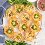 A plate of crispy wonton cups filled with jalapeno popper dip and topped with fresh jalapeno slices.