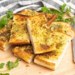 A pile of toasted garlic bread on a wooden cutting board.