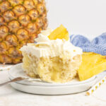A slice of vanilla cake, filled with pineapple pudding, topped with crushed pineapple and vanilla whipped topping.