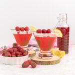 Two raspberry martinis garnished with fresh berries and lemon wedges.