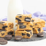 A stack of Oreo blondies on a slate plate with a small bottle of milk.