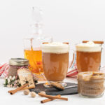 Two mugs of hot buttered rum topped with whipped cream, a bottle of rum in the background.