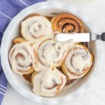 Six cinnamon rolls with frosting in a round pie dish.