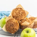 A pile of apple muffins with crumb topping in parchment muffin liners.