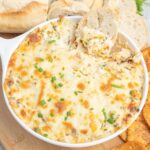 Cheesy leek dip in a small casserole dish with sliced baguette.