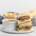 Beef sandwich on hoagie roll cut in half and stacked with a bowl of gravy.