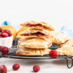 Round cranberry handpies in a stack with one broke open showing cranberry sauce inside.