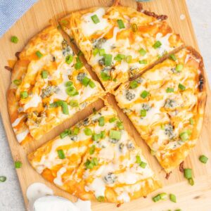 A buffalo chicken flatbread pizza cut into wedges on a cutting board.