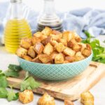 A bowl of croutons and a bottles of oil and vinegar salad dressing.