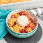 A serving of cherry pineapple dump cake in a small bowl with a scoop of vanilla ice cream.