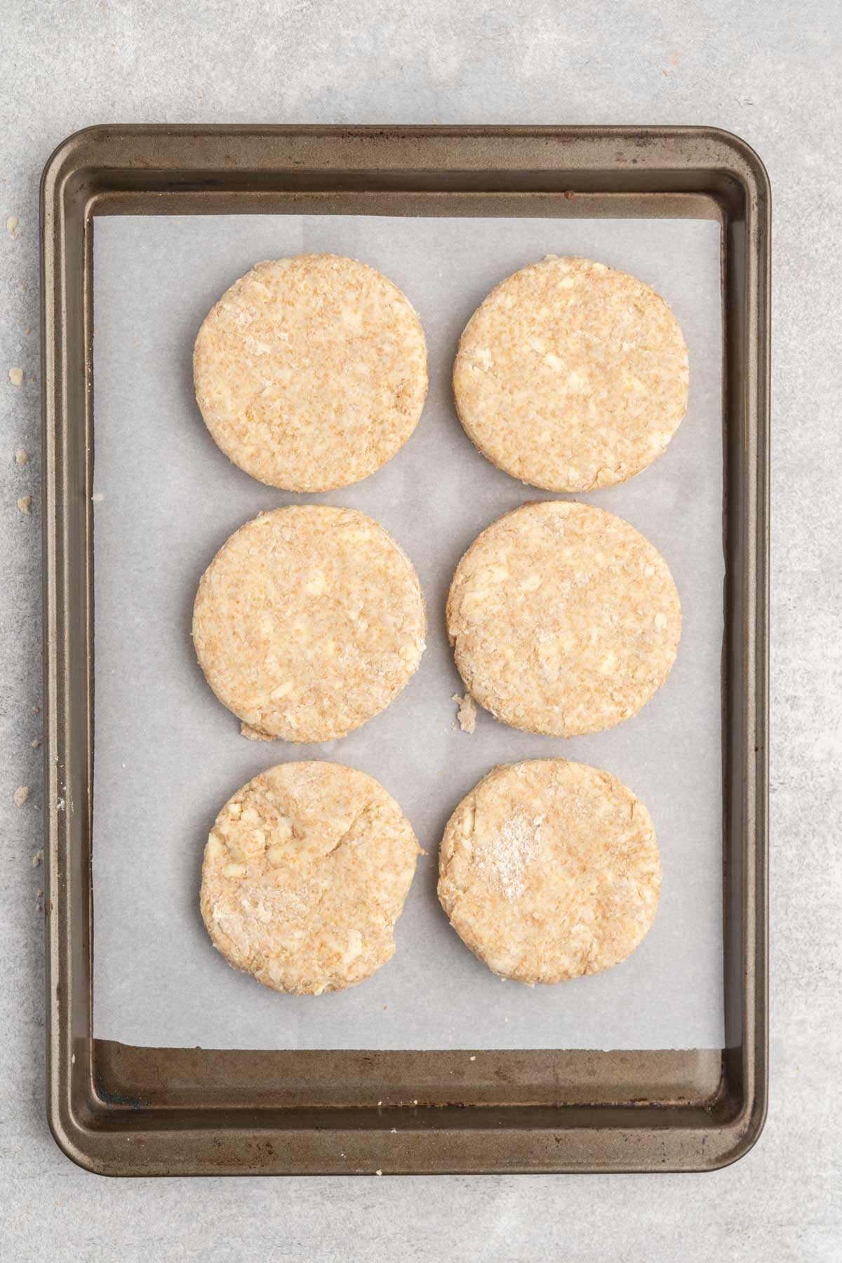 Biscuit rounds on a parchment lined baking sheet before baking.