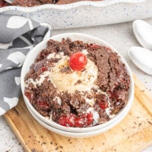 Chocolate cherry dump cake in a small bowl topped with vanilla ice cream and a cherry.